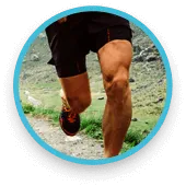 Άντρας τρέχει σε εξωτερικό χώρο με αθλητικά ρούχα, μυώδη πόδια και φυσικό περιβάλλον στο φόντο.